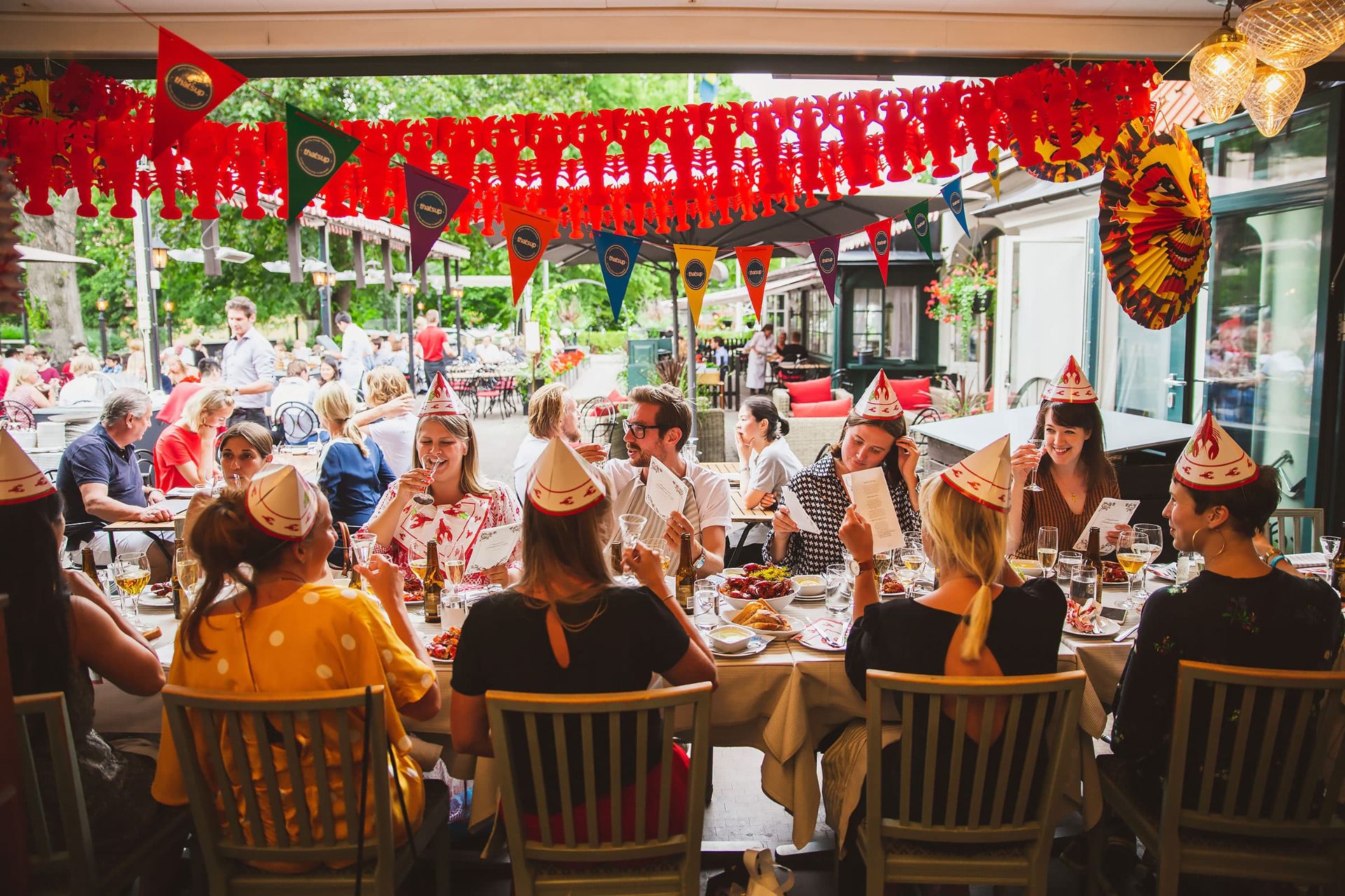 Friends in paper party hats laughing together at a long crayfish table
