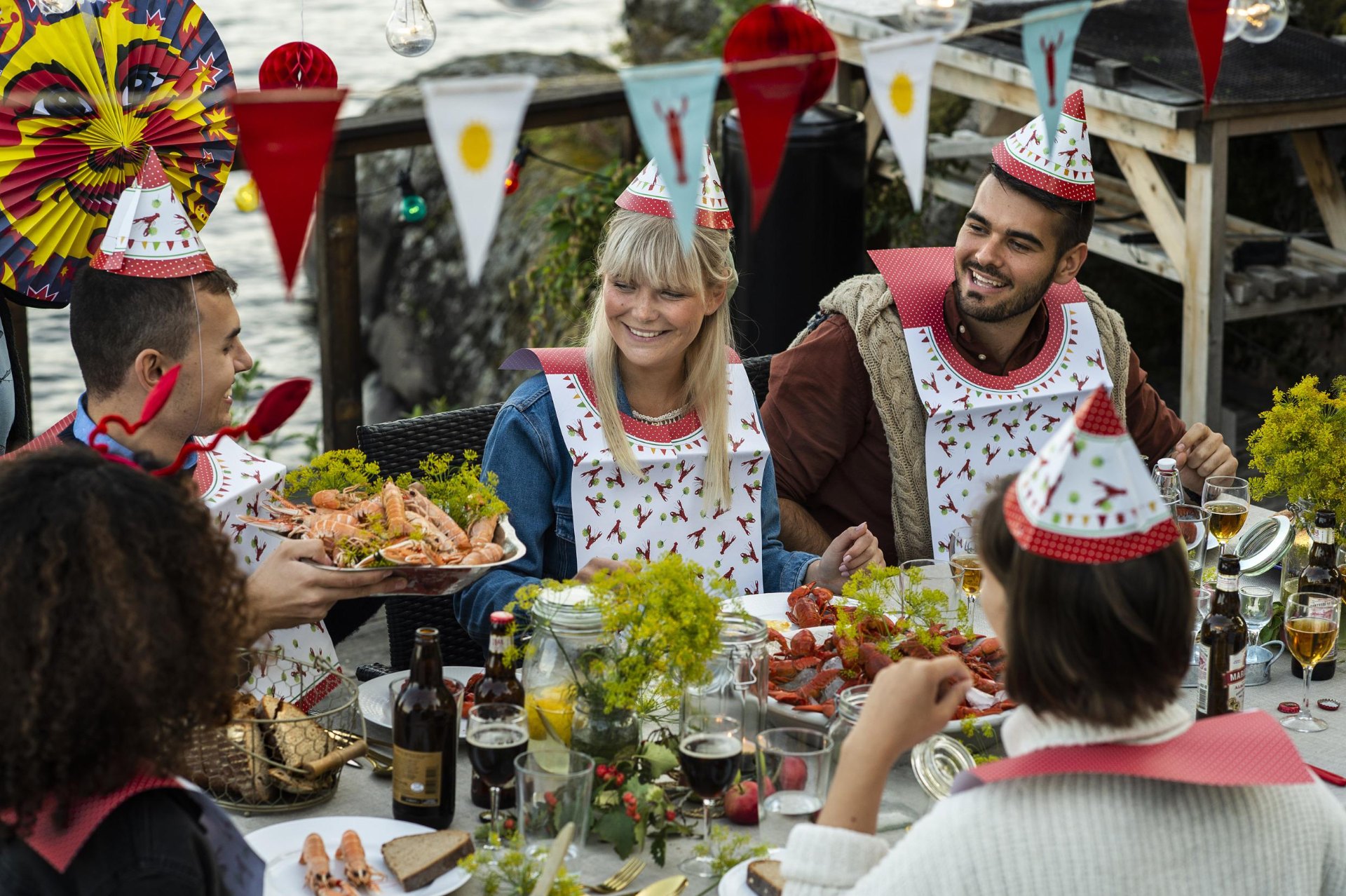 Friends in crayfish party hats laughing and sharing a meal outdoors