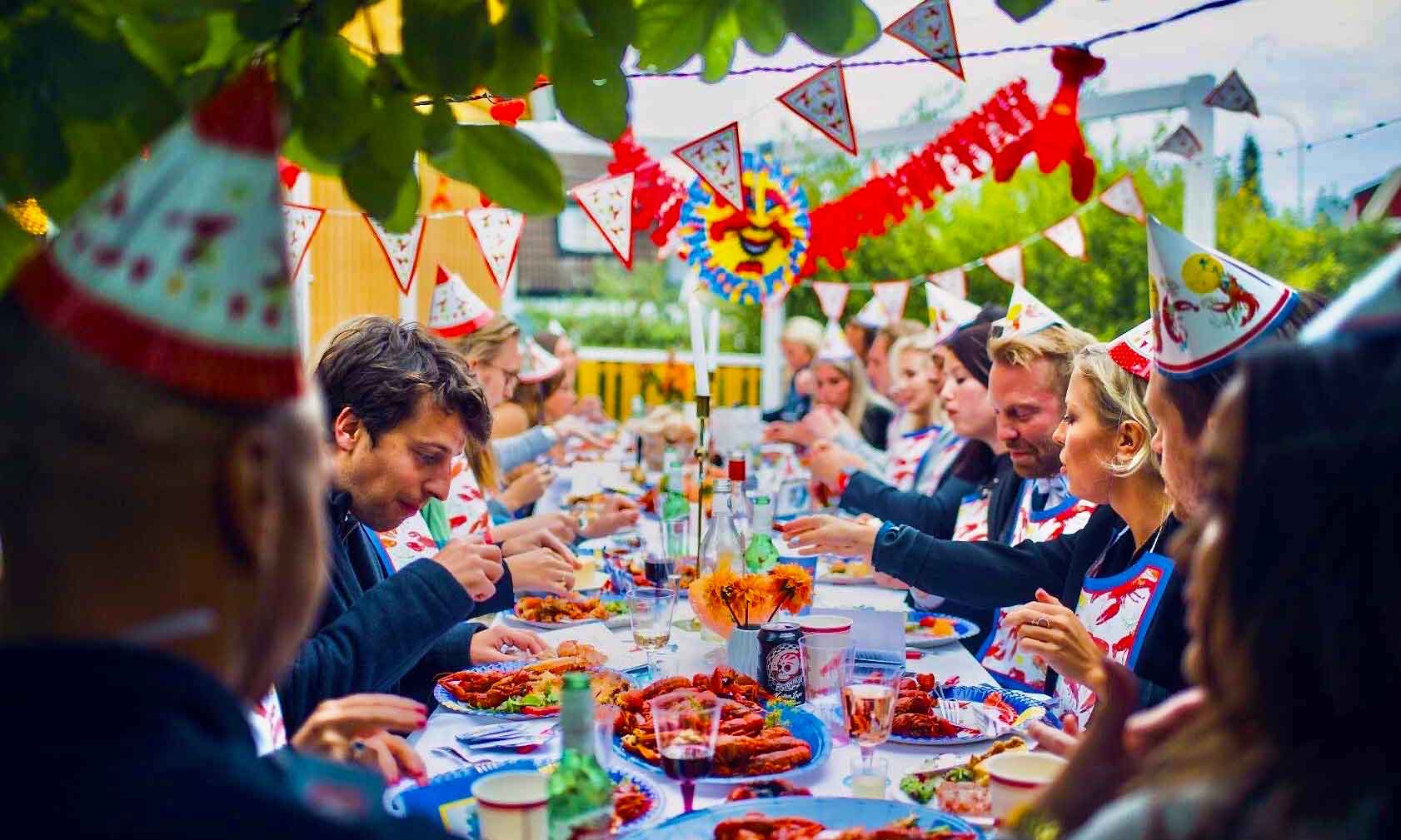 A long outdoor table of guests in party hats under crayfish banners